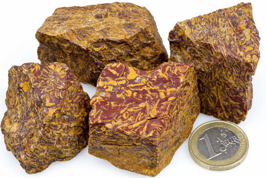 Four raw jasper specimens with red and yellow swirled patterns on a white surface, next to a one-euro coin.