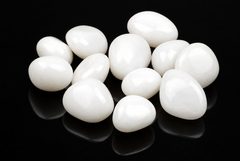 A group of smooth, white quartz stones arranged on a dark reflective surface.