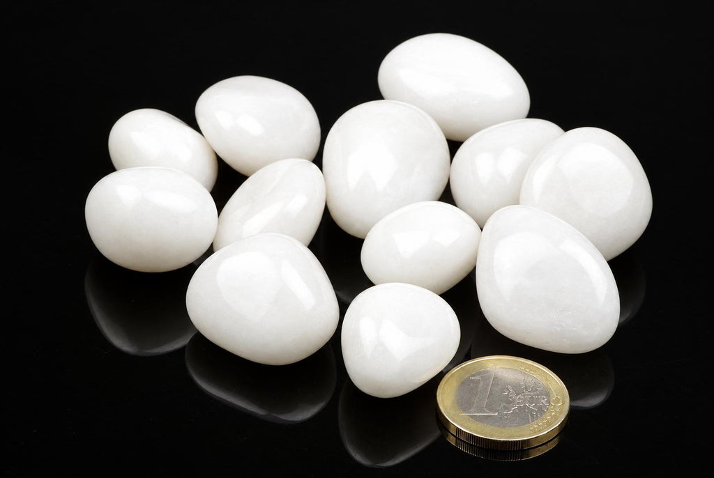A group of smooth, white stones on a dark surface with a one-euro coin for scale.