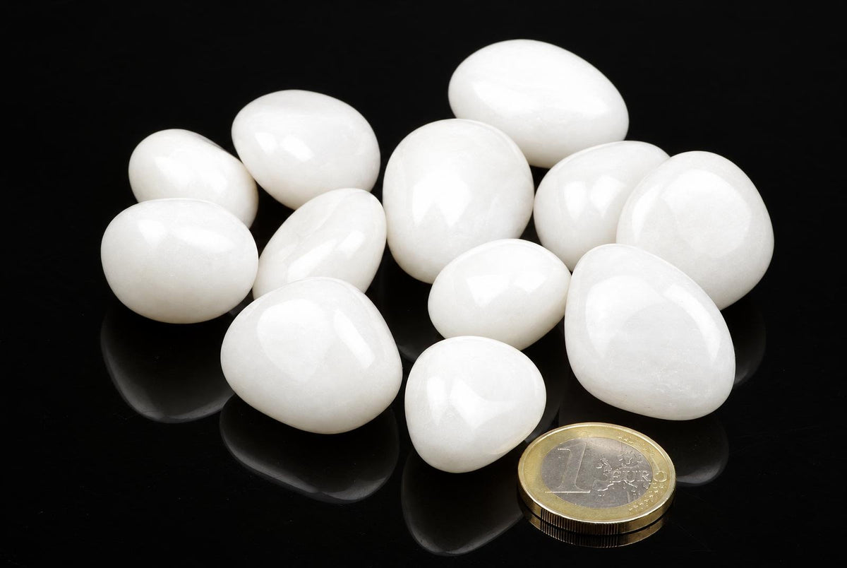 A group of smooth, white stones on a dark surface with a one-euro coin for scale.