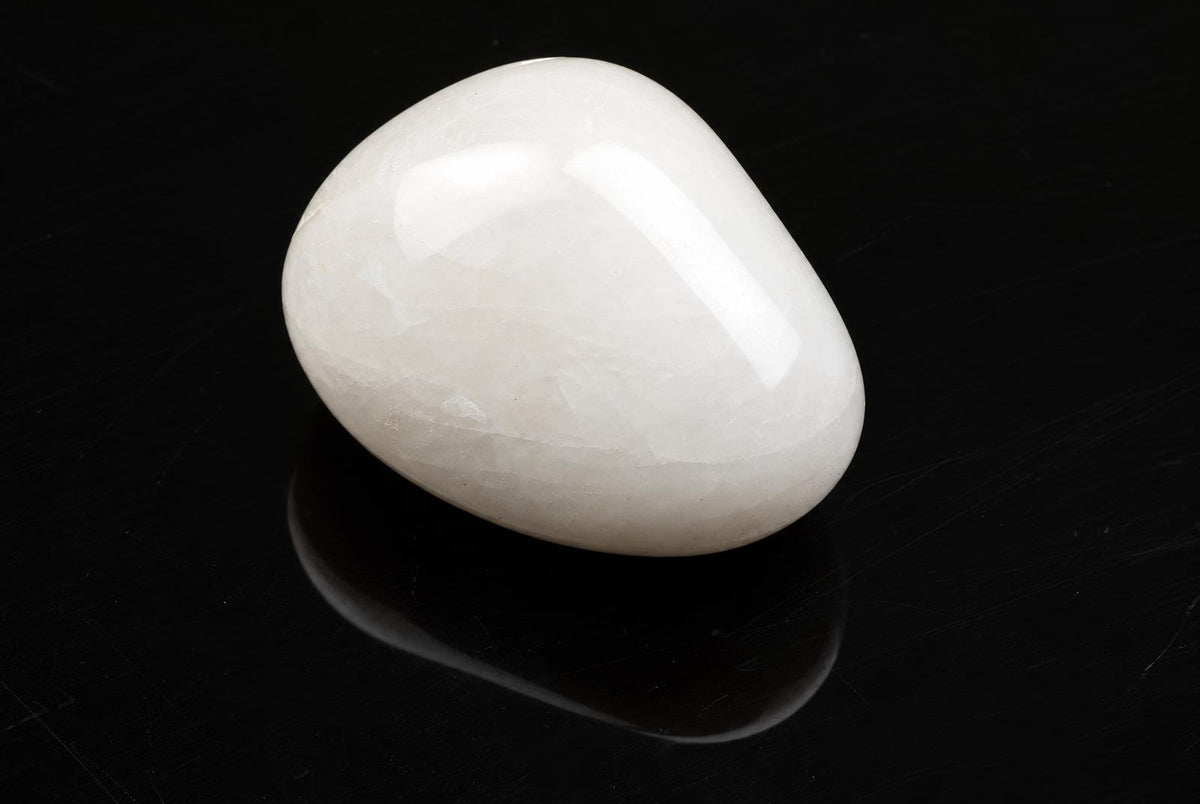 A smooth, polished white stone with a rounded shape rests on a dark surface.