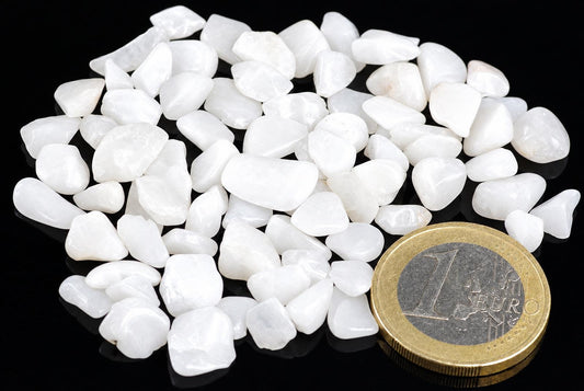 A pile of small, white, polished quartz stones on a dark surface next to a one euro coin.
