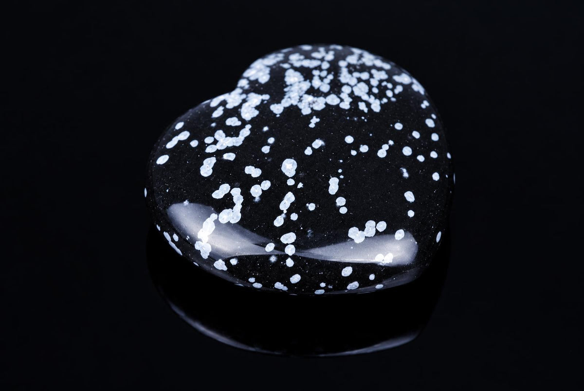 A heart-shaped black stone with white speckles rests on a dark, reflective surface.