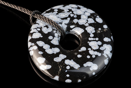 A polished, donut-shaped pendant with a black base and white snowflake patterns, threaded on a dark cord against a black background.
