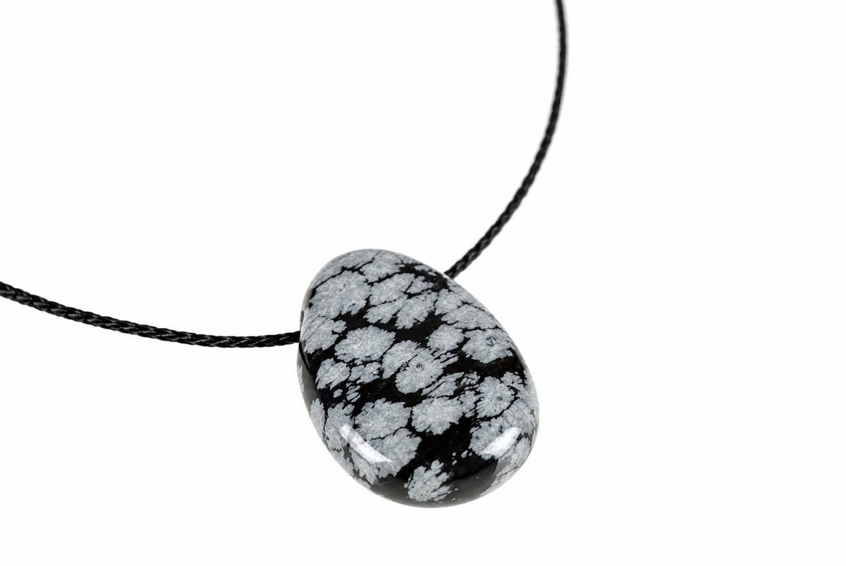 A polished black pendant with white snowflake patterns hangs from a dark cord against a plain background.