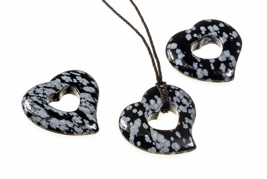 Three heart-shaped pendants with black and white speckled patterns, one on a dark cord against a white background.