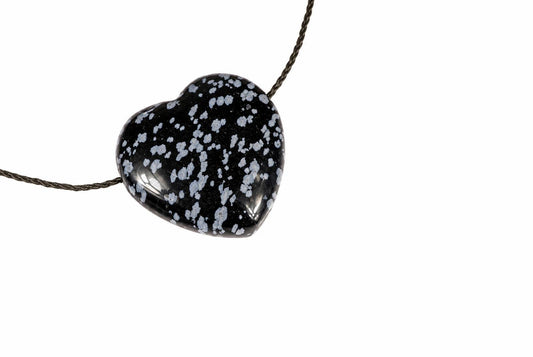 A heart-shaped pendant with a black base and white speckles hangs from a dark cord against a plain white background.