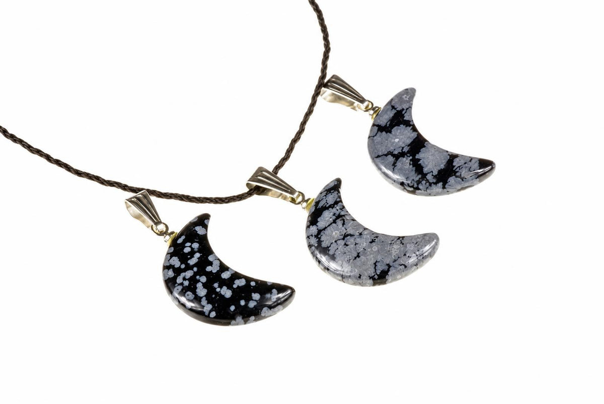 Three crescent-shaped pendants with black and white speckled stones on dark cords against a white background.