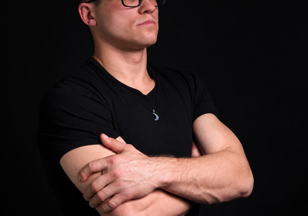 A man in a black t-shirt wears a silver-toned crescent moon pendant on a dark surface.