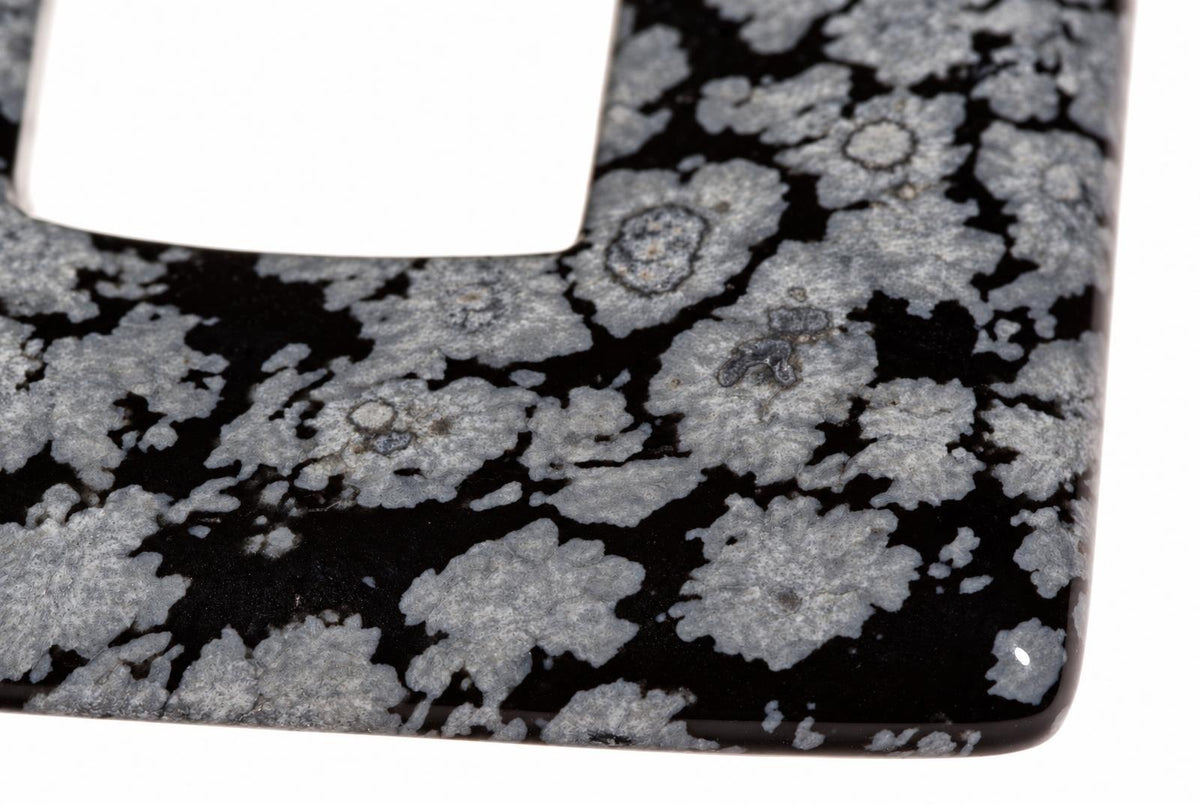 A close-up of a square pendant with a black and grey snowflake obsidian pattern on a white background.