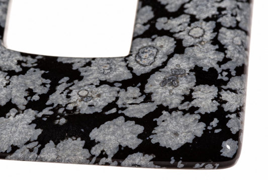 A close-up of a square pendant with a black and grey snowflake obsidian pattern on a white background.