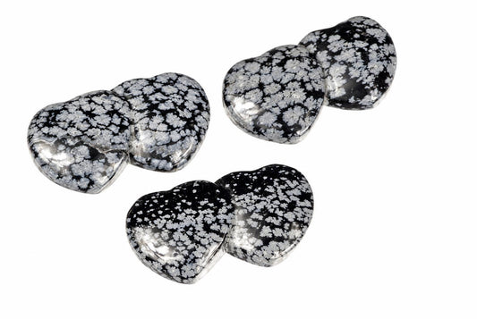 Three polished heart-shaped stones with black and white snowflake patterns on a pale surface.
