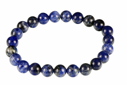 A bracelet of round beads in deep blue and black sodalite, arranged on a white surface.