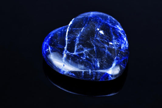 A polished sodalite stone shaped like a heart, featuring deep blue and white veining on a dark reflective surface.