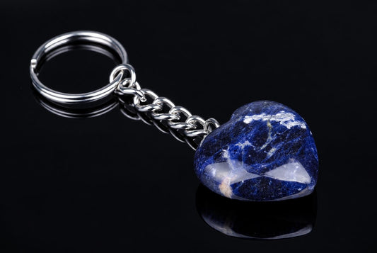 A silver-toned keychain with a heart-shaped sodalite pendant, featuring deep blue and white patterns, on a dark reflective surface.