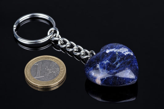 A silver-toned keychain with a heart-shaped sodalite pendant, blue and white, on a dark reflective surface.