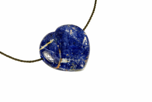 A heart-shaped sodalite pendant with deep blue, white and gold-coloured veins on a dark cord against a pale surface.