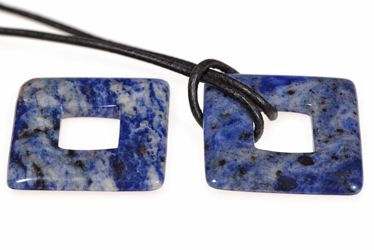 Two square sodalite pendants with central holes, blue and white speckled, on a black cord against a white background.