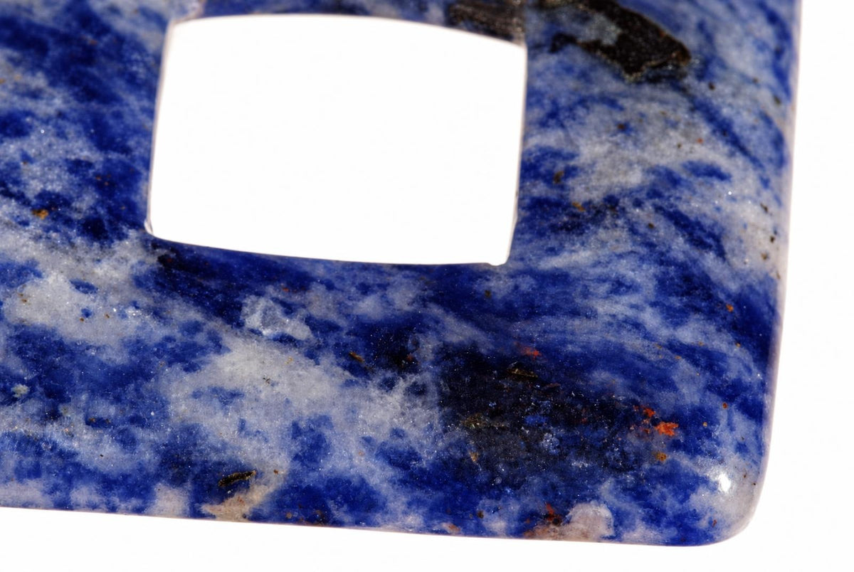 A close-up of a polished sodalite pendant with deep blue and white swirled patterns, featuring a square cutout on a dark surface.
