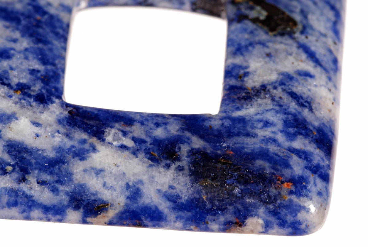 A close-up of a square sodalite pendant with a central hole, showing blue and white mottled patterns on a dark surface.