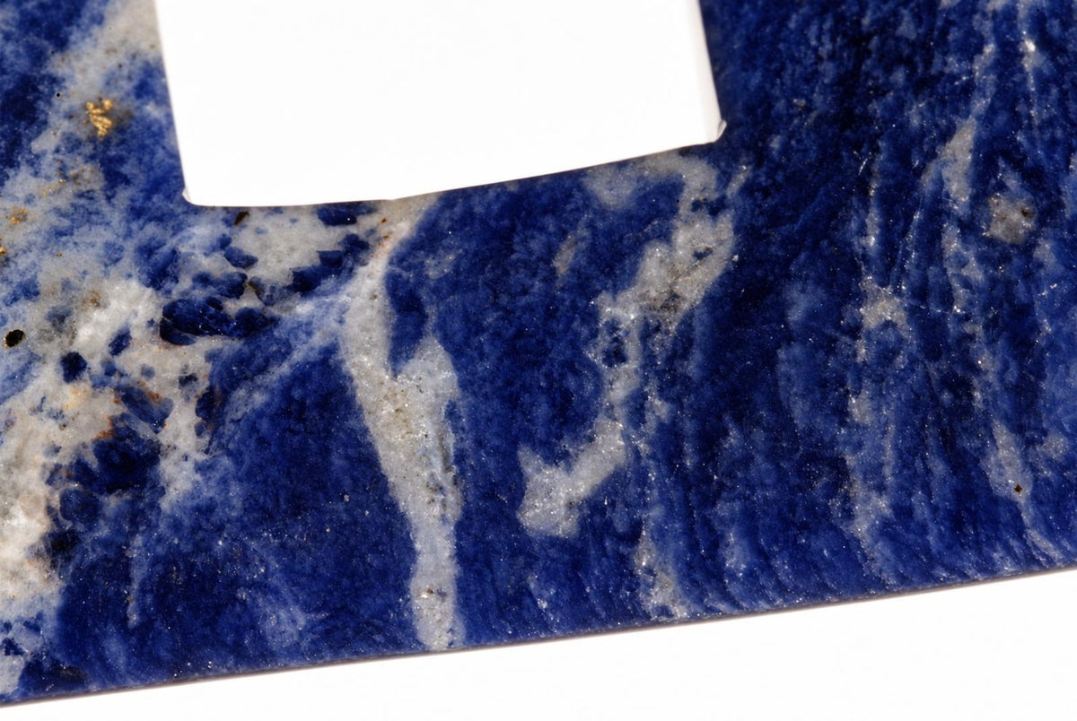 A close-up of a polished sodalite stone showing deep blue and white swirled patterns on a dark surface.