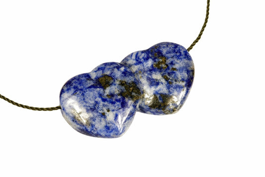 A blue pendant formed from two joined hearts with pale and dark mottled markings lies with its cord on a white background.