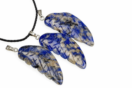 Three blue and white sodalite pendants shaped like wings, each with engraved lines, attached to a black cord on a pale surface.