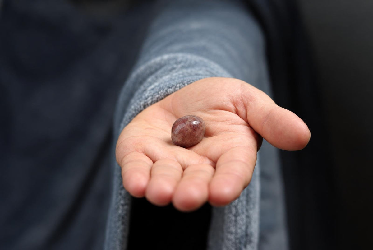 A hand holds a small, smooth, reddish-brown polished stone on a dark surface.