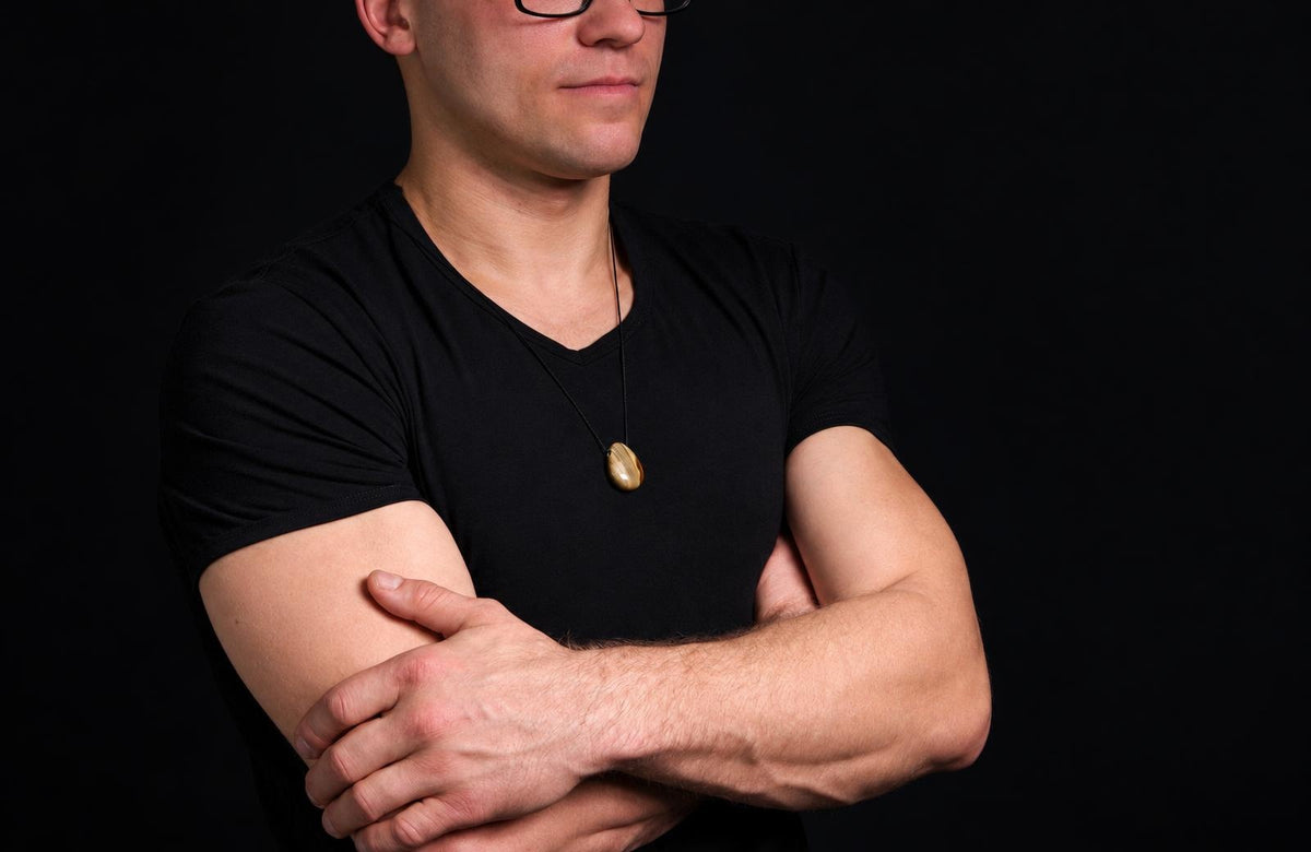 A man in a black shirt wears a gold-coloured oval pendant on a dark surface.