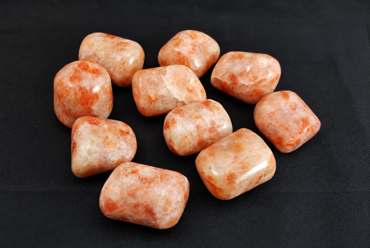 Nine polished sunstone tumbled stones with orange and cream patterns on a dark surface.