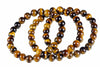 Overlapping loops of glossy round golden-brown and dark beads rest on a white surface.