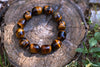 A bracelet of polished tiger eye beads with golden and dark brown stripes rests on a wooden stump outdoors.