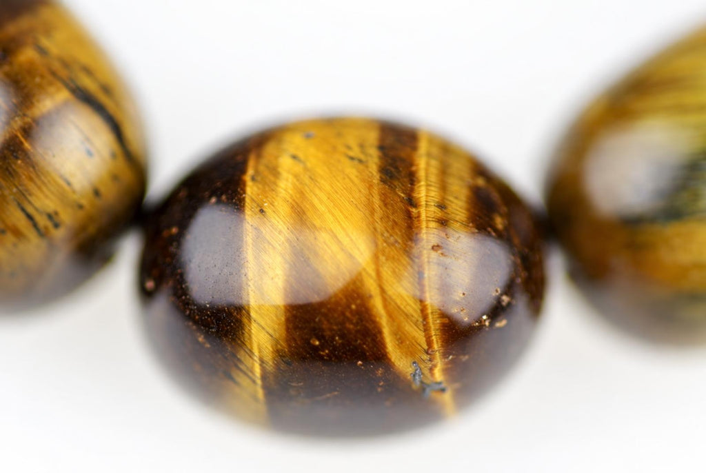 Close-up of a round tiger eye bead with golden and dark brown stripes, set on a white surface.