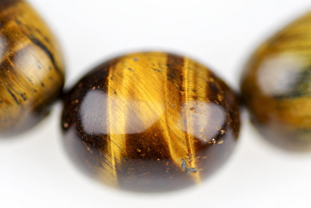 Close-up of a round tiger eye bead with golden and dark brown stripes, set on a white surface.