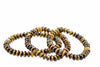 Overlapping bracelets of small flattened golden-brown beads with dark bands lie on a white background.