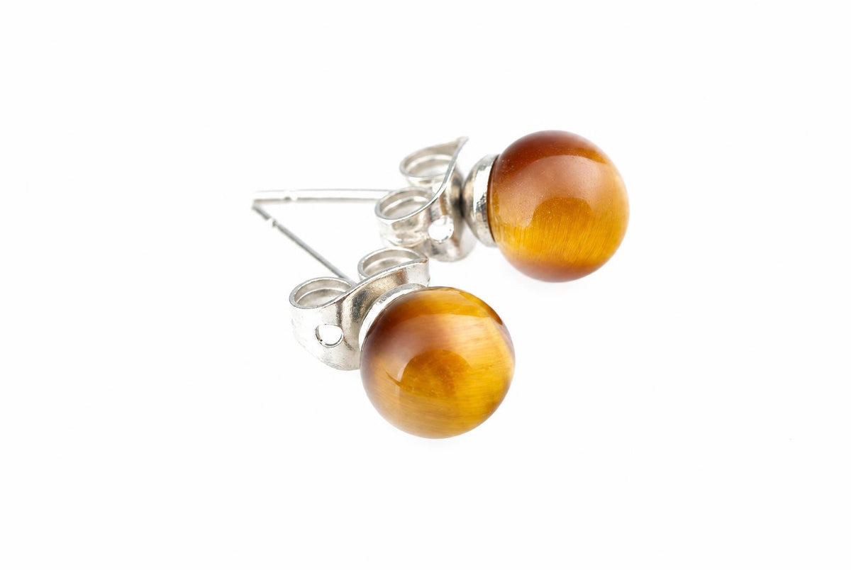 Two round golden-yellow and brown stud earrings with silvery butterfly backs lie on a white background.