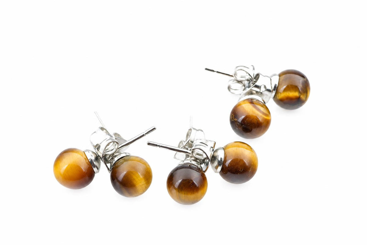 Three pairs of round golden-yellow and brown stud earrings with silvery posts lie on a white surface.