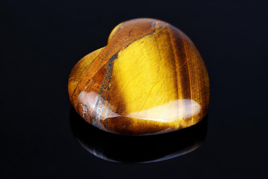 A polished, heart-shaped stone with yellow and brown stripes on a dark surface.
