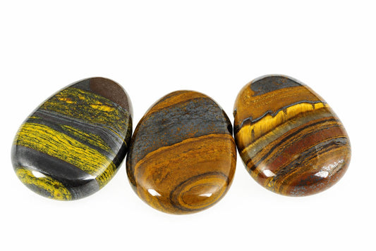 Three polished tiger eye stones with yellow, brown and dark stripes arranged on a white surface.