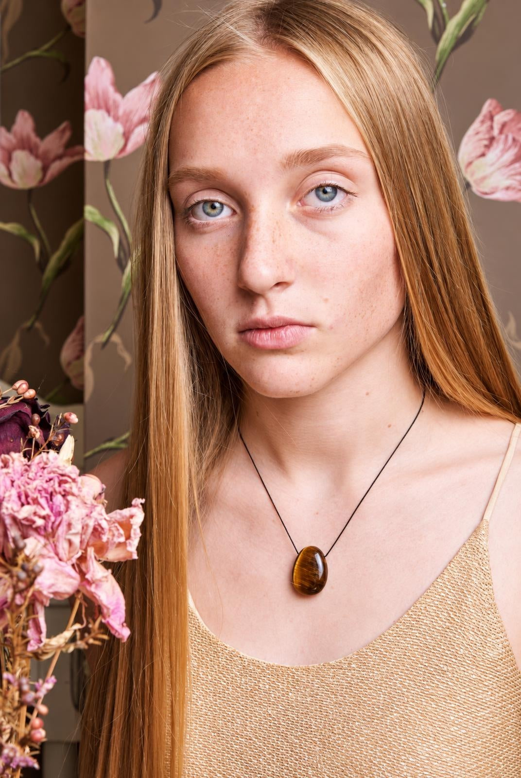 A woman wears a black cord necklace with an oval, polished brown pendant on a pale surface.