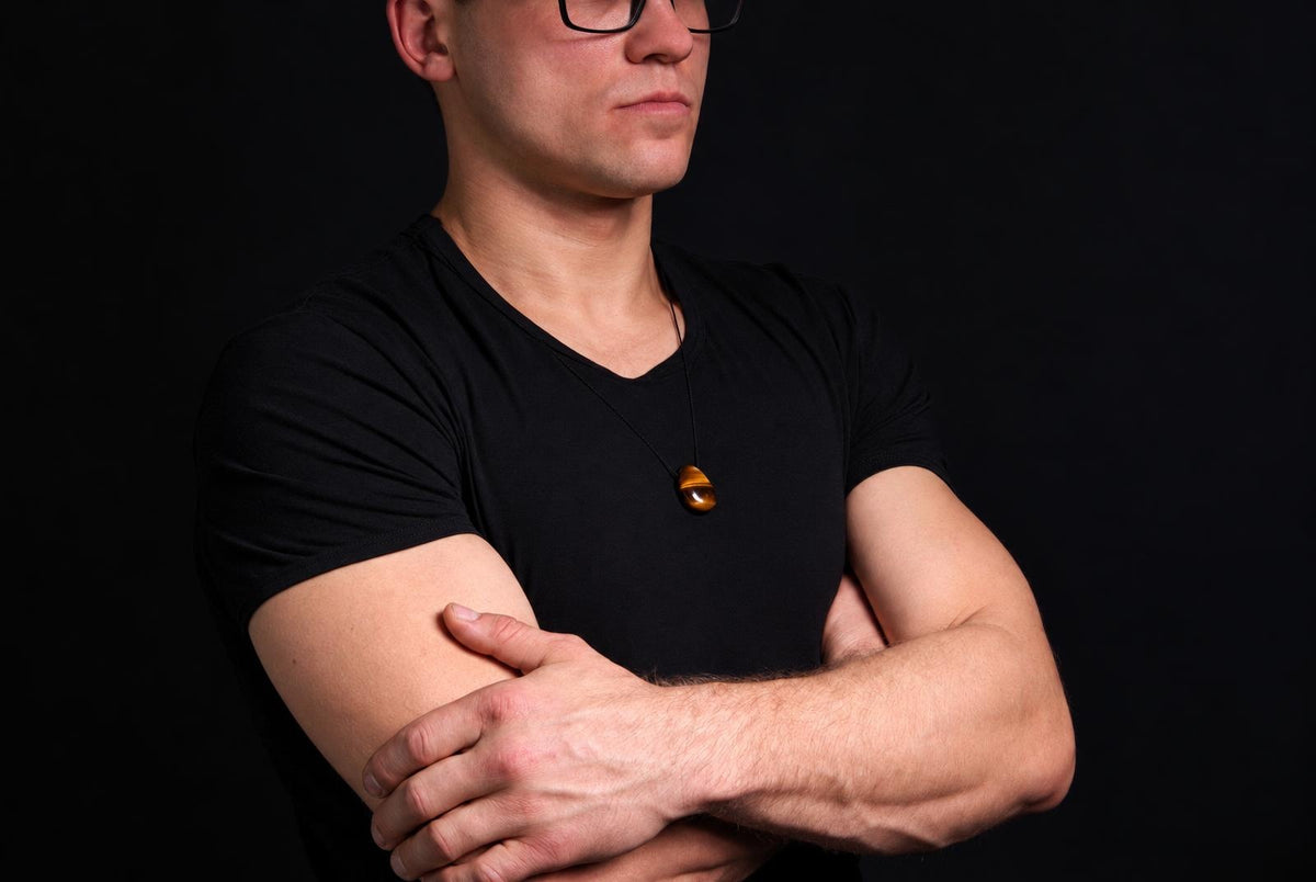A man in a black shirt wears a dark brown, polished drop-shaped pendant on a thin cord against a dark background.