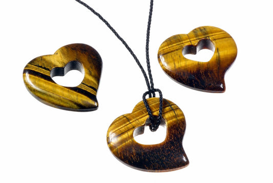 A black cord passes through a polished tiger eye heart pendant beside matching pendants on a white background.