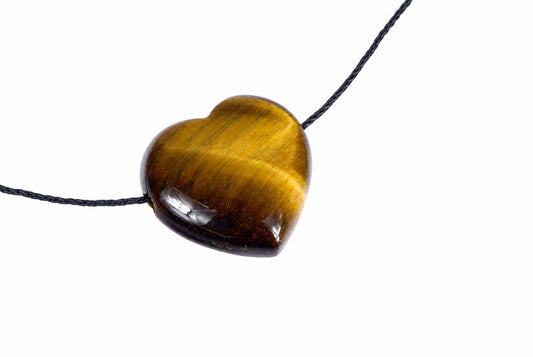 A heart-shaped pendant made of polished tiger eye stone with golden-brown stripes, threaded on a dark cord against a white background.