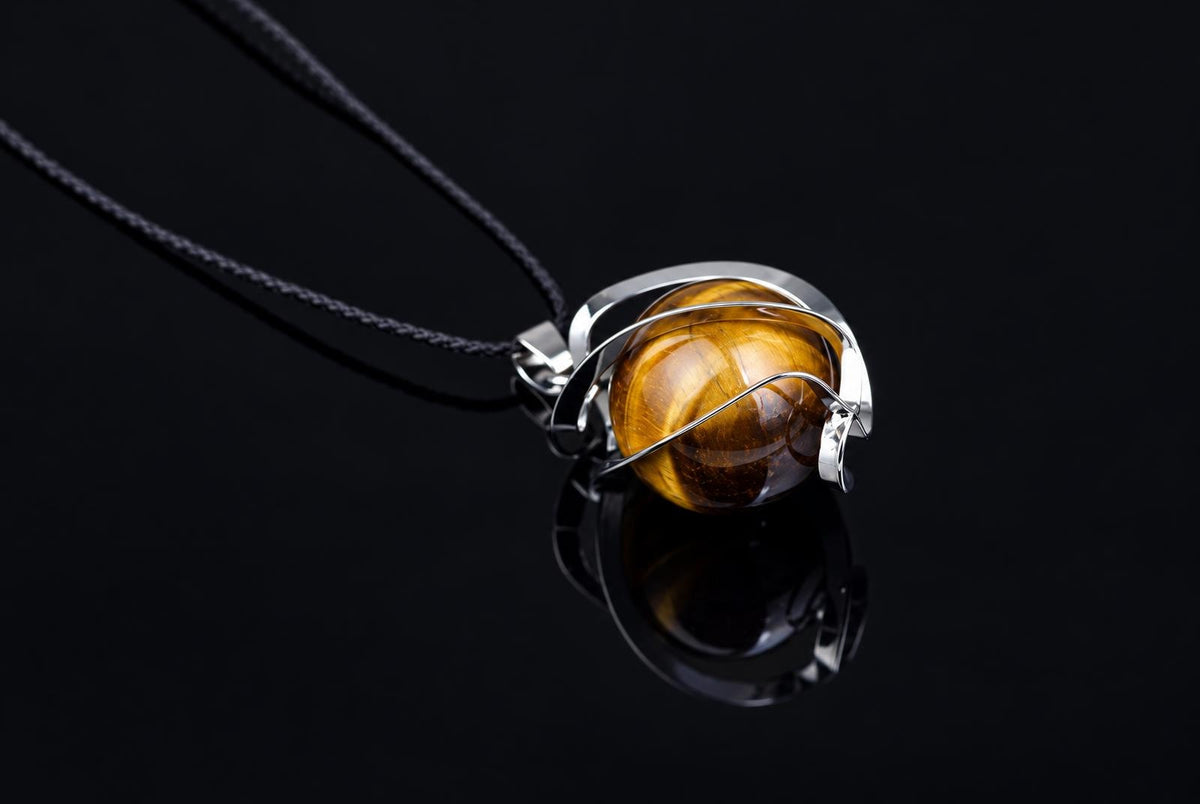 A silver-toned wire-wrapped pendant with a round, golden-brown tiger eye stone hangs from a black cord on a dark surface.