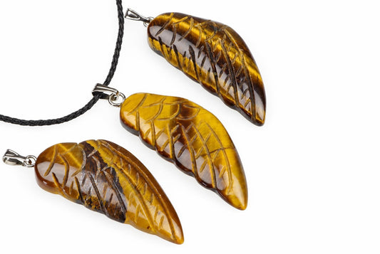 Three carved tiger eye pendants shaped like wings, each with a silver-toned bail and one on a black cord, arranged diagonally on a white surface.
