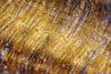 Close-up of a tiger eye stone showing golden brown and dark brown banding with visible cracks on a dark surface.