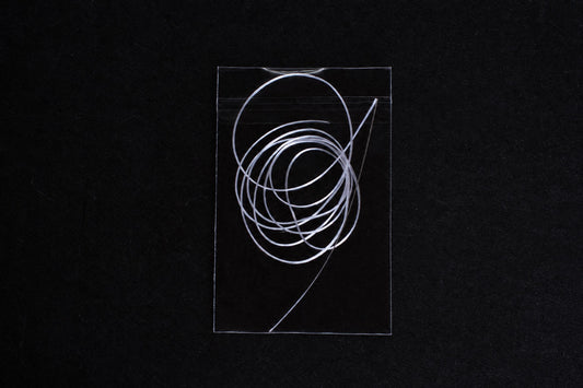 A tangled coil of clear, flexible tubing inside a transparent plastic bag on a dark surface.