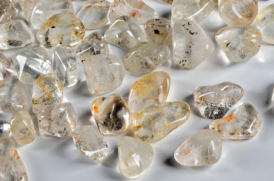 A pile of polished, translucent Topaz stones with brown and black inclusions on a pale surface.