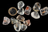 A collection of clear, translucent rough stones with dark and brown inclusions on a black surface next to a two-euro coin.