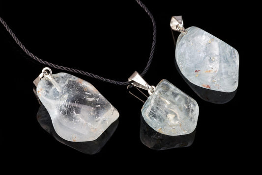 Three silver-toned pendants with pale blue, translucent stones on a dark surface against black background.